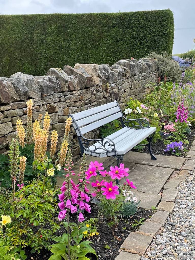 Garden bench among flowers with a dry stone wall